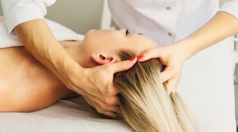 Beautician cosmetologist makes a relaxing head and hair massage professional procedure in a beauty clinic salon for client